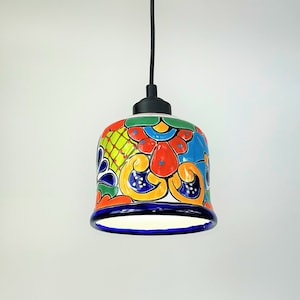 May include: A colorful ceramic pendant light with a black cord and ceiling mount. The light features a bell-shaped shade with a vibrant floral pattern in shades of blue, red, yellow, and green.