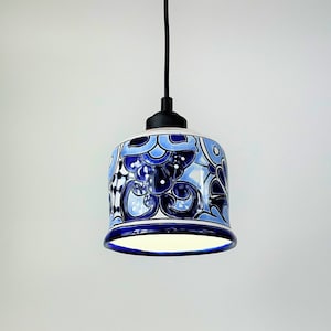 May include: A blue and white ceramic pendant light with a floral pattern hangs from a black cord and ceiling fixture.
