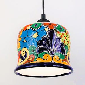 May include: A colorful ceramic pendant light with a floral design in shades of blue, green, yellow, orange, and red. The light has a white interior and a dark blue rim.