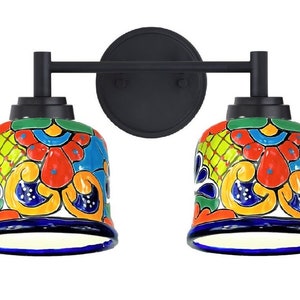 May include: A black metal wall sconce with two colorful ceramic bell-shaped shades. The shades feature a traditional Mexican Talavera design with blue, green, yellow, orange, and red floral patterns.