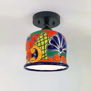May include: A colorful ceramic ceiling light fixture with a black metal base and a white interior. The ceramic shade features a traditional Mexican Talavera design with blue, green, yellow, orange, and red floral patterns.