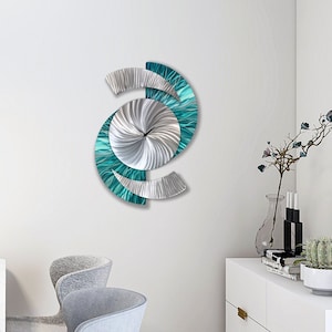 Può includere: Un orologio da parete moderno con un design turchese e argento. Il quadrante dell'orologio è un design argentato a spirale con accenti turchesi. Le lancette dell'orologio sono nere.