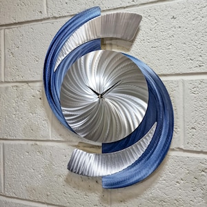 Può includere: Un orologio da parete moderno con un design in metallo argento e blu. Il quadrante dell'orologio è un design argentato a spirale con lancette nere.