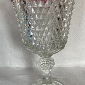 May include: Clear glass goblet with a ruby red rim. The goblet features a diamond-cut pattern on the bowl and a detailed stem. The base is round and the glass is transparent.