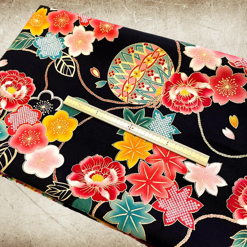 K&ouml;nnte beinhalten: Schwarzer Stoff mit einem sich wiederholenden Muster aus roten, rosa und gelben Blumen, goldenen Bl&auml;ttern und einer goldenen und gr&uuml;nen Kugel. Der Stoff ist mit goldenen seilartigen Designs verziert.