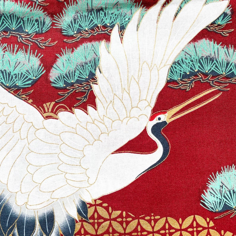 Puede incluir: Una gr&uacute;a blanca con las alas extendidas sobre un fondo rojo con un patr&oacute;n dorado y verde. La gr&uacute;a tiene un pico largo y delgado y una mancha roja en la cabeza.