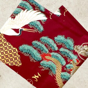 Puede incluir: Tela roja con una gr&uacute;a dorada y blanca, pinos verdes y dorados y un dise&ntilde;o de drag&oacute;n dorado.