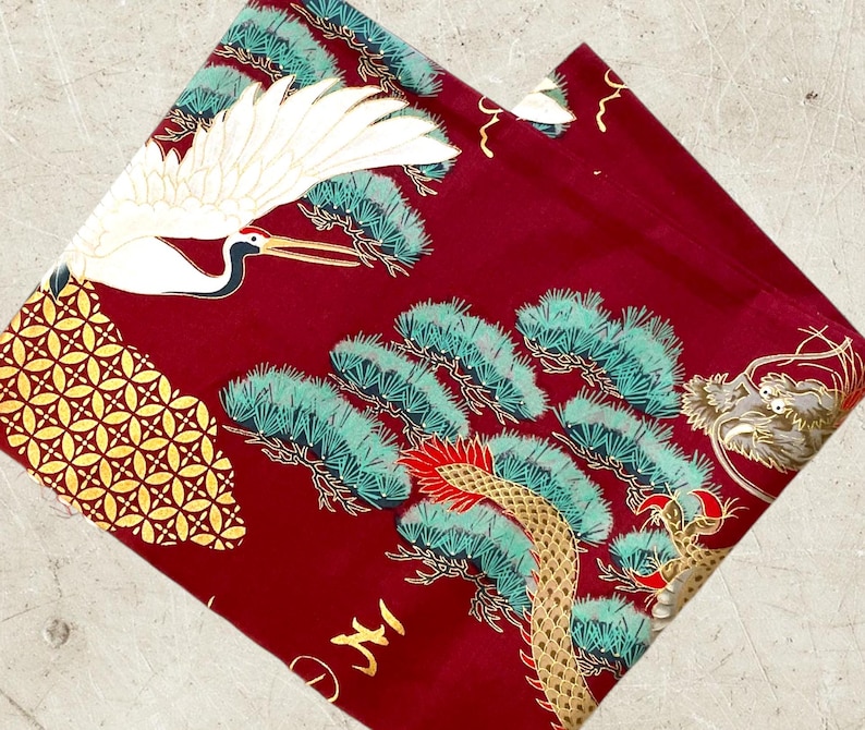 Puede incluir: Tela roja con una gr&uacute;a dorada y blanca, pinos verdes y dorados y un dise&ntilde;o de drag&oacute;n dorado.