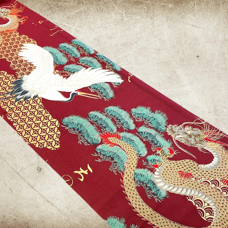 Puede incluir: Tela roja con un dise&ntilde;o de drag&oacute;n y gr&uacute;a dorado y blanco. El drag&oacute;n est&aacute; enroscado alrededor de un pino con hojas verdes. La gr&uacute;a est&aacute; volando sobre el &aacute;rbol. El fondo es una tela roja con un patr&oacute;n geom&eacute;trico dorado y blanco.