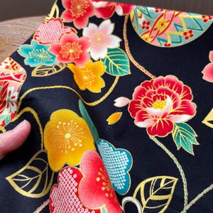K&ouml;nnte beinhalten: Schwarzer Stoff mit einem sich wiederholenden Muster aus goldenen, roten und gelben Blumen. Die Blumen sind stilisiert und haben ein traditionelles japanisches Design. Der Stoff ist perfekt zum Quilten, N&auml;hen oder Basteln.