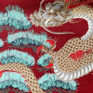 Puede incluir: Una tela roja con un dise&ntilde;o de drag&oacute;n dorado y blanco. El drag&oacute;n est&aacute; enroscado alrededor de un motivo de pino. La tela tiene una superficie texturizada.