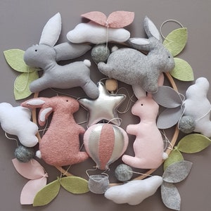 May include: A baby mobile with a wooden ring, featuring felt clouds, leaves, stars, a hot air balloon, and bunnies in pink and gray.