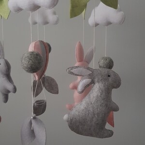 May include: A wooden baby mobile with a gray and pink bunny, a hot air balloon, clouds, leaves, and a silver star.