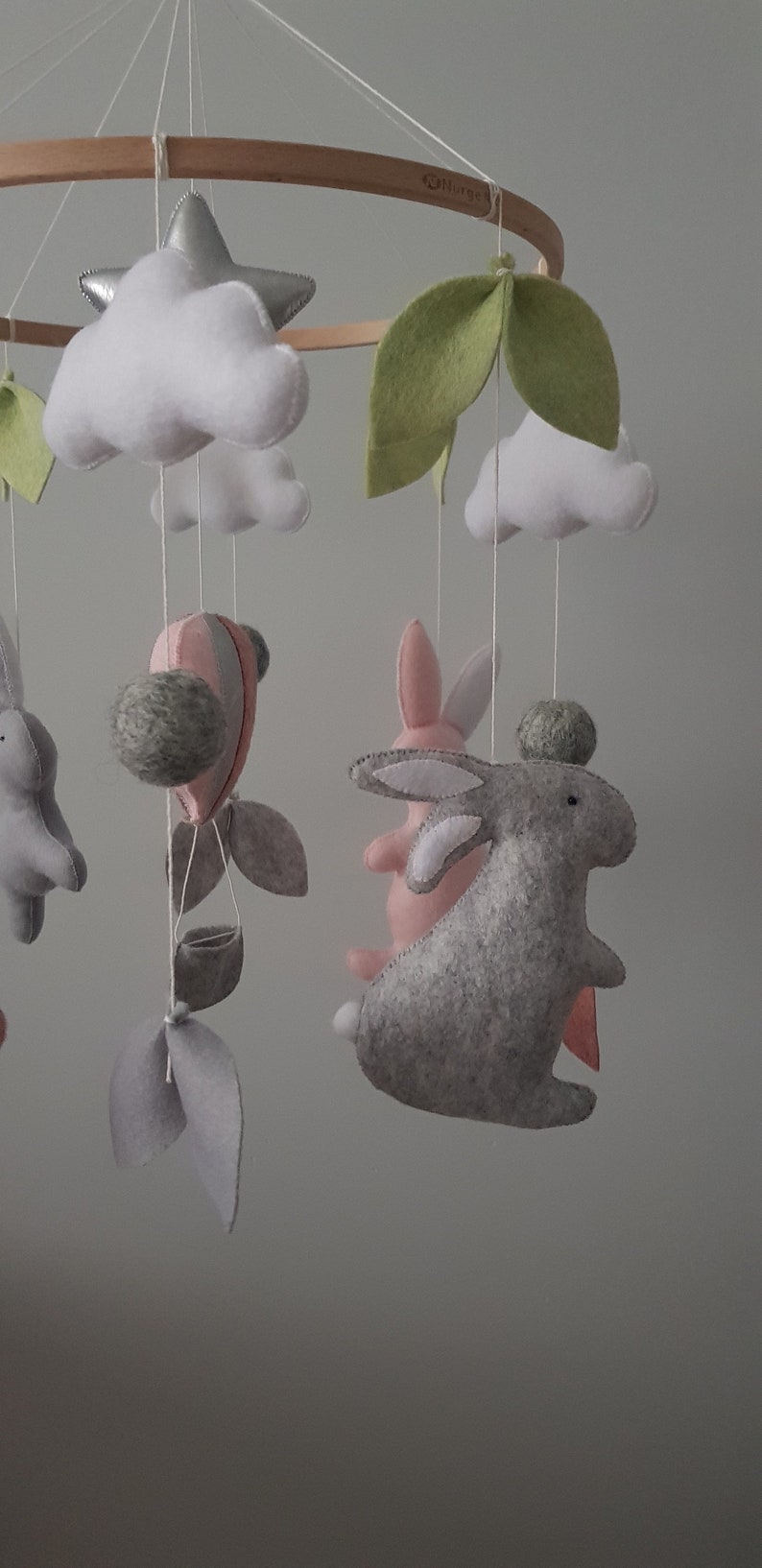 May include: A wooden baby mobile with a gray and pink bunny, a hot air balloon, clouds, leaves, and a silver star.