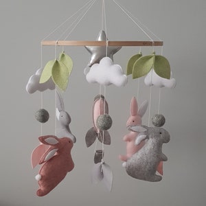 May include: A baby mobile with a wooden ring, white clouds, green leaves, a silver star, and four felt bunnies in pink and gray.
