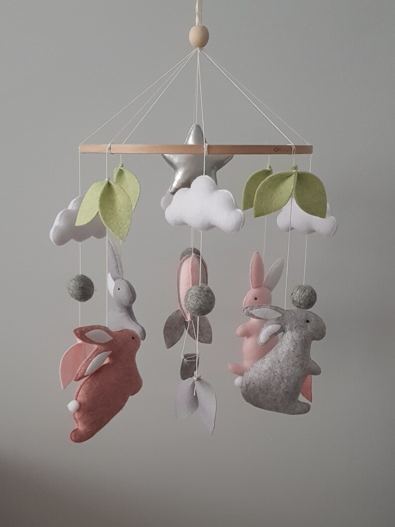 May include: A baby mobile with a wooden ring, white clouds, green leaves, a silver star, and four felt bunnies in pink and gray.