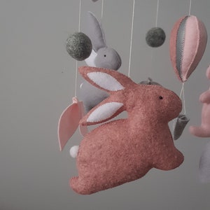 May include: A pink and gray felt baby mobile with a pink bunny, a gray bunny, clouds, leaves, a star, and a hot air balloon.