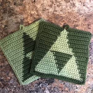 May include: Two green crocheted pot holders with a triangular pattern. The pot holders are made with different shades of green yarn.