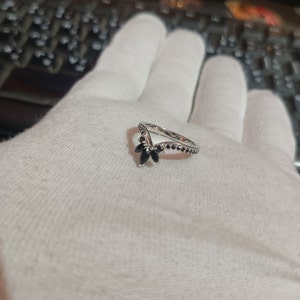 May include: A silver ring with a V-shaped band and black gemstones. The ring is set with five black gemstones in a flower shape.