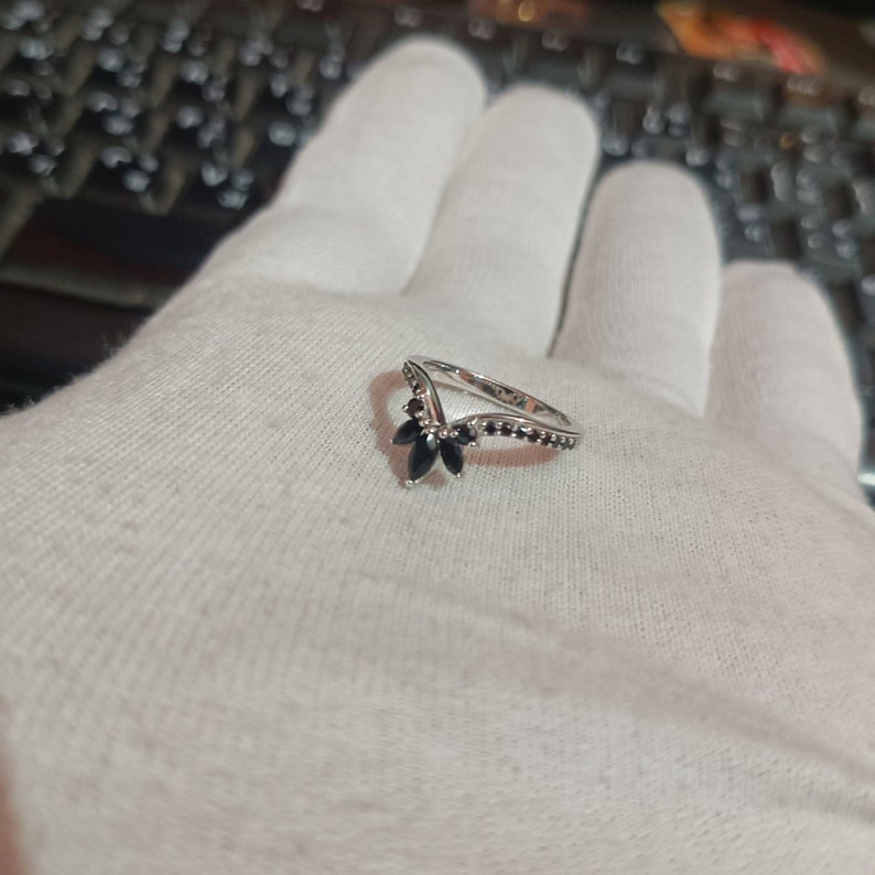 May include: A silver ring with a V-shaped band and black gemstones. The ring is set with five black gemstones in a flower shape.
