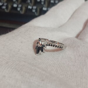 May include: A silver ring with a V-shaped design and black gemstones. The ring is set with small black stones along the band and larger black stones in the V-shaped design.