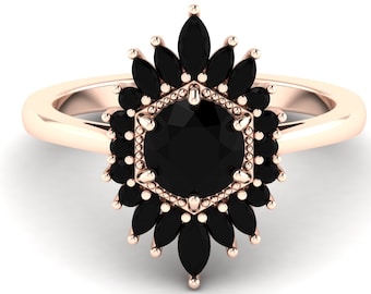 May include: A rose gold ring with a large black gemstone surrounded by a halo of smaller black gemstones. The ring has a hexagonal setting with a delicate, ornate design.
