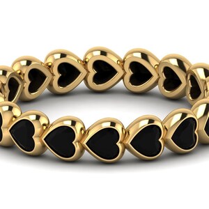May include: A gold band ring with a row of black heart-shaped stones.