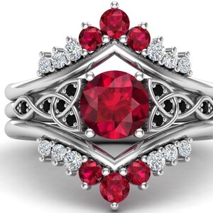 May include: A three-piece ruby and diamond engagement ring set. The centre ring features a large ruby surrounded by a Celtic knot design with black diamonds. The two side rings feature a row of diamonds and rubies.