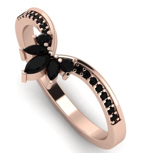May include: A rose gold ring with a black marquise-shaped gemstone set in the center. The ring is accented with smaller black gemstones around the band.