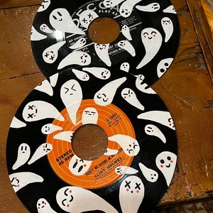 May include: Two black vinyl records with white ghost illustrations painted on them. The top record has the text "PLAY 45" and "GUY LOMBARDO AND" on it. The bottom record has the text "STEREO 45 RPM" and "THERE'S NO FUTURE IN MY STOMACH" on it.