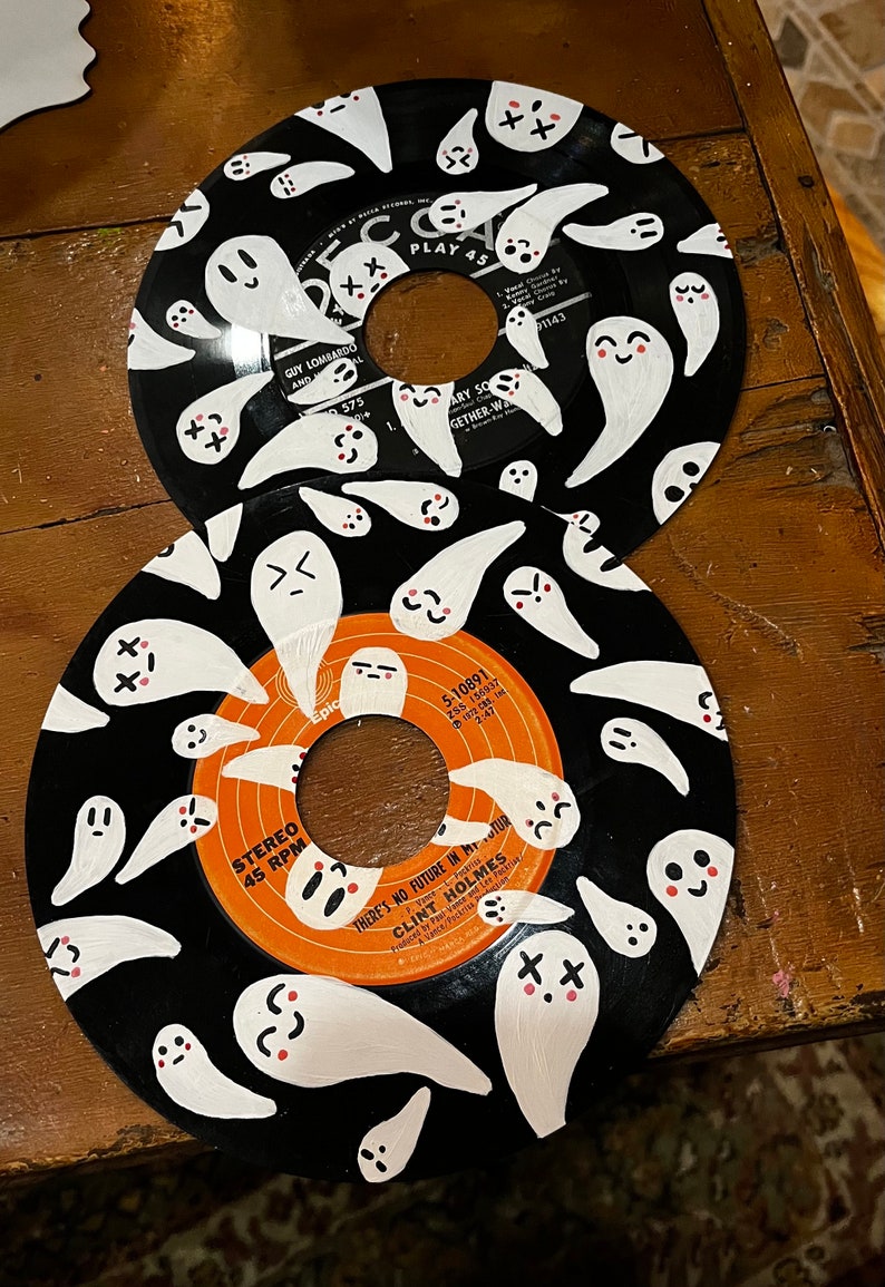 May include: Two black vinyl records with white ghost illustrations painted on them. The top record has the text "PLAY 45" and "GUY LOMBARDO AND" on it. The bottom record has the text "STEREO 45 RPM" and "THERE'S NO FUTURE IN MY STOMACH" on it.