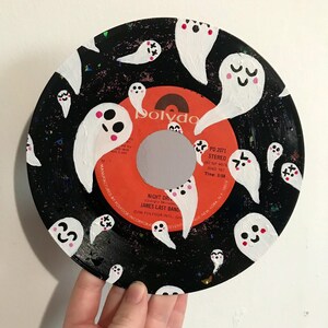 May include: A black vinyl record painted with white ghosts. The ghosts have pink cheeks and some have eyes. The record label is orange and says "Polydor" in black letters. The record is titled "Night Drive" by "James Last Band".