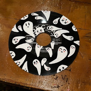 May include: A black vinyl record with a white design of ghosts with pink accents. The record has the text "PLAY 45" and "GUY LOMBARDO AND AL 575" printed on it.