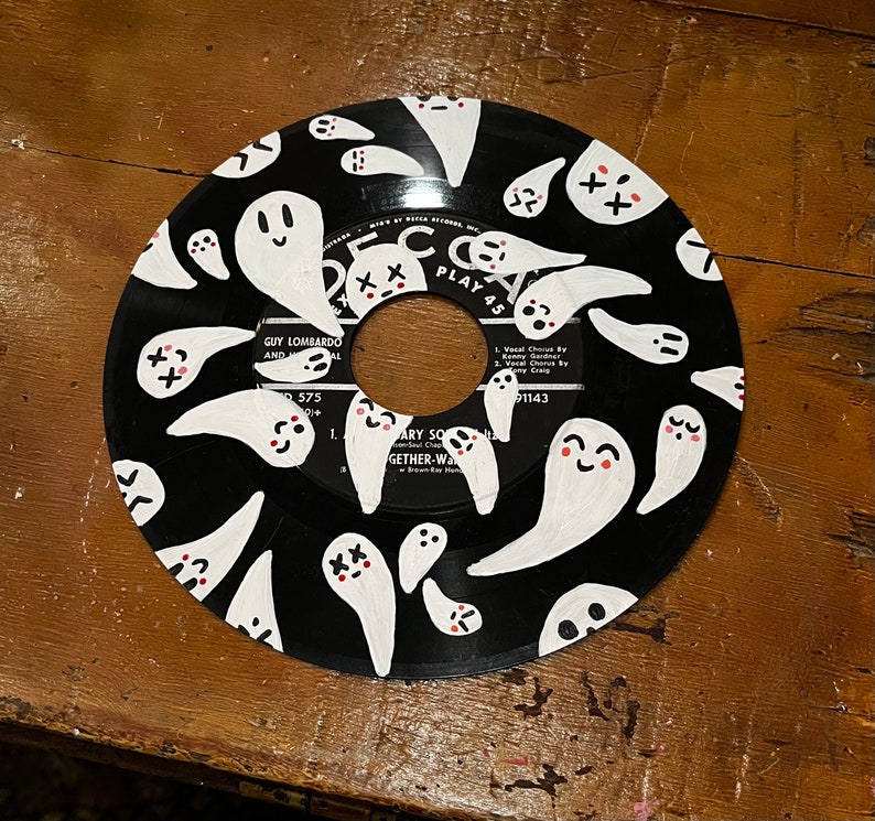 May include: A black vinyl record with a white design of ghosts with pink accents. The record has the text "PLAY 45" and "GUY LOMBARDO AND AL 575" printed on it.