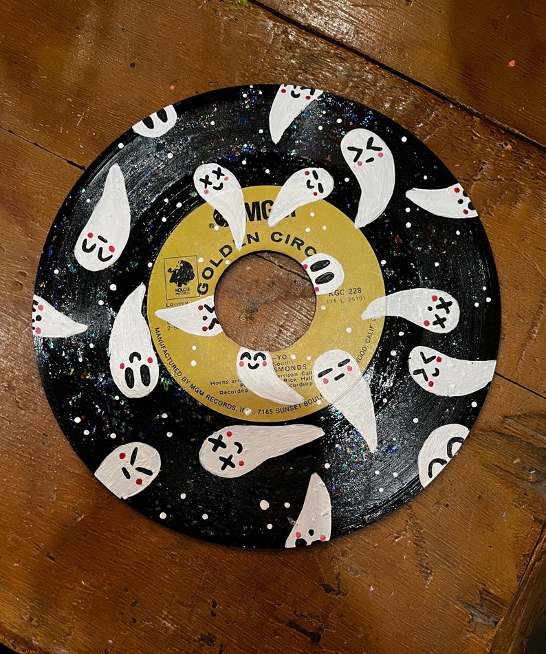 May include: A black vinyl record with a gold label that says "Golden Circle" and "KGC 228". The record is painted with white ghosts with red and black details. The ghosts have different expressions.