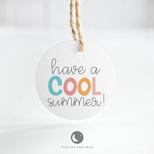 Puede incluir: Una etiqueta redonda blanca con una cuerda de yute marrón colgando de la parte superior. La etiqueta tiene el texto "have a COOL summer!" escrito en negro con la palabra "COOL" en letras de colores.