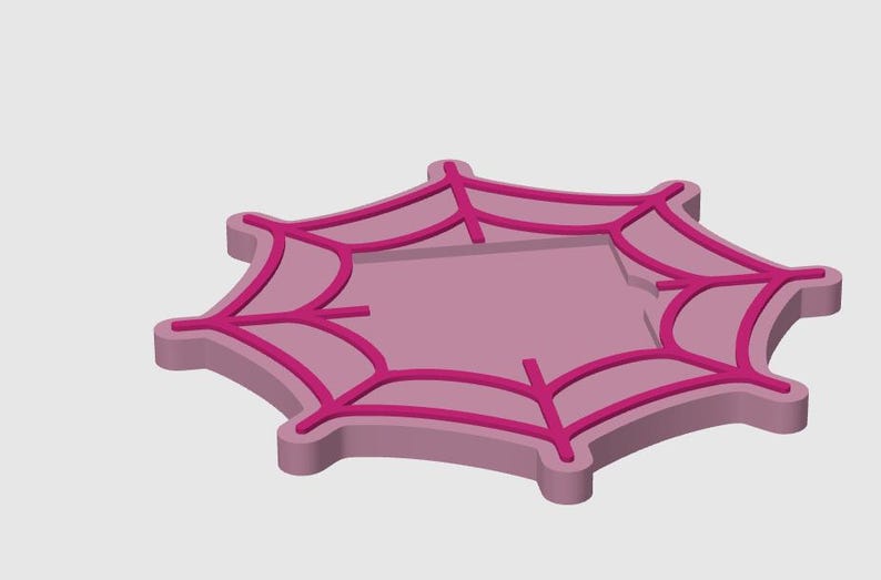 May include: A pink and magenta spiderweb-shaped object. The object has a raised border and a web design in a darker shade of pink. The design is a stylized representation of a spider's web.