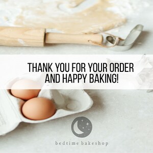 May include: A white countertop with baking supplies, including a rolling pin, cookie cutters, a carton of eggs, and a handwritten sign that reads "THANK YOU FOR YOUR ORDER AND HAPPY BAKING!" The sign is above a white carton of eggs with a gray moon and stars logo that reads "bedtime bakeshop".