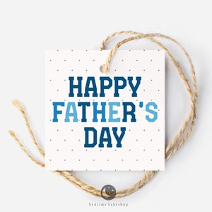 以下が含まれることがあります： 白地に小さな黒い点のあるギフトタグ。青と白の文字で「Happy Father's Day」と書かれている。茶色の紐で結ばれている。
