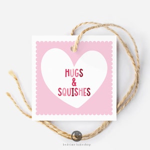May include: Pink gift tag with a white heart shape and the text "Hugs & Squishes" in red and pink lettering.