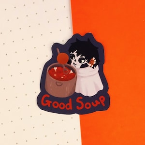 May include: A sticker featuring a cartoon character with a skull face, black hair, and a white cloak, holding a pot of red soup. The text "Good Soup" is written in red on a blue background.