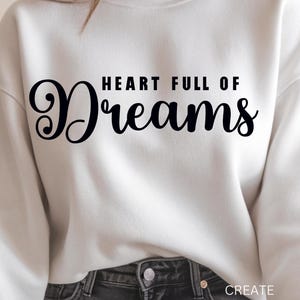 May include: A white sweatshirt with the text "HEART FULL OF Dreams" in black script. The words "CREATE WITH KAREN" are printed in white at the bottom right. The sweatshirt is paired with dark gray jeans.