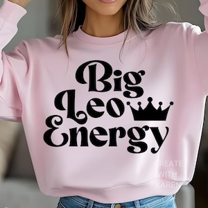 Puede incluir: Sudadera rosa claro con la frase "Big Leo Energy" en negro, en negrita, coronada por una corona negra. El texto "CREATE WITH KAREN" está impreso en blanco en la parte inferior derecha.