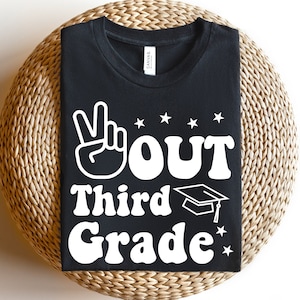Könnte beinhalten: Schwarzes T-Shirt mit weißem Text und Grafiken. Der Text lautet "✌️OUT Third Grade" mit einem Friedenszeichen, Sternen und einer Abschlusskappe. Das Shirt wird auf einer gewebten, kreisförmigen Oberfläche präsentiert.