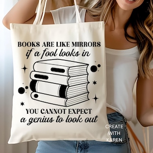 May include: Cream-colored tote bag with the quote "BOOKS ARE LIKE MIRRORS if a fool looks in YOU CANNOT EXPECT a genius to look out" in black text. The design includes a stack of books and star and circle accents.