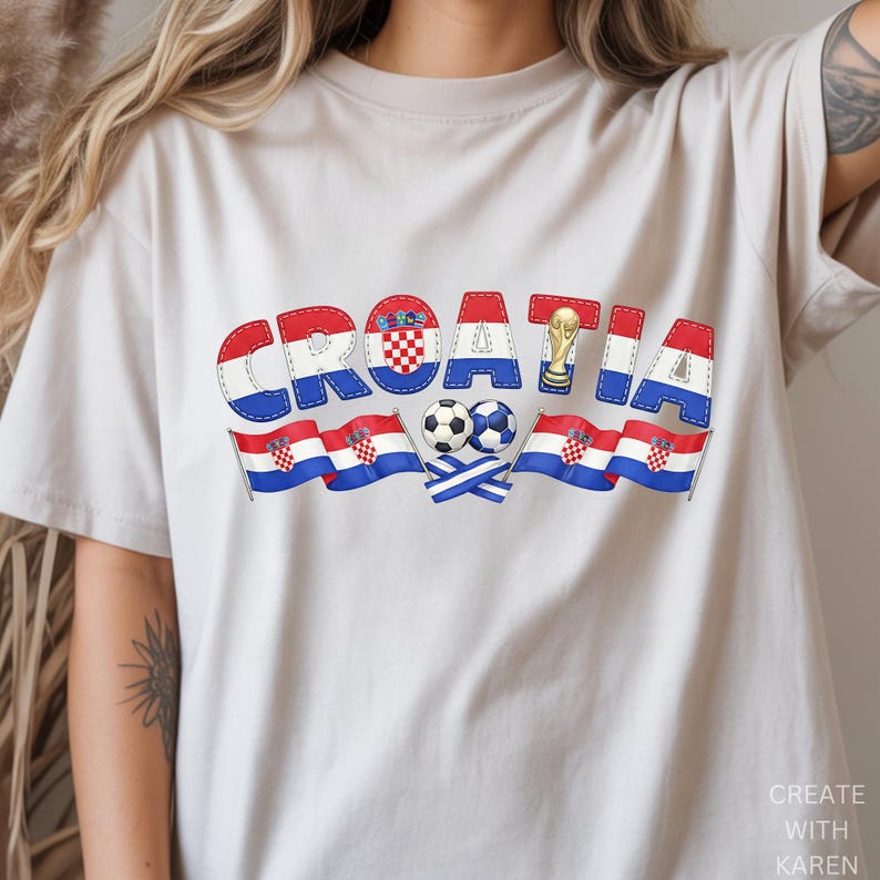 May include: A beige t-shirt featuring the word "CROATIA" in a stitched, patriotic design. The design incorporates the Croatian flag colors, a soccer ball, and a gold trophy. Two Croatian flags and two soccer balls are also featured.