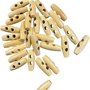 May include: A collection of light brown wooden toggle buttons, each featuring a cylindrical shape with two holes drilled through the centre. These fasteners are arranged in a scattered pattern, showcasing the natural grain and smooth texture.