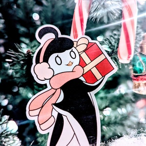 May include: A cartoon penguin wearing a pink scarf and earmuffs holds a red gift box with a white ribbon. The penguin is standing in front of a Christmas tree with a candy cane.