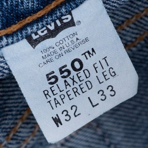 Może przedstawiać: Biała metka dżins&oacute;w Levi's z czarnym tekstem. Metka zawiera napis "550 TM Relaxed Fit Tapered Leg W32 L33". Zawiera r&oacute;wnież napis "100% Bawełna Wyprodukowano w USA. Instrukcja pielęgnacji na odwrocie".