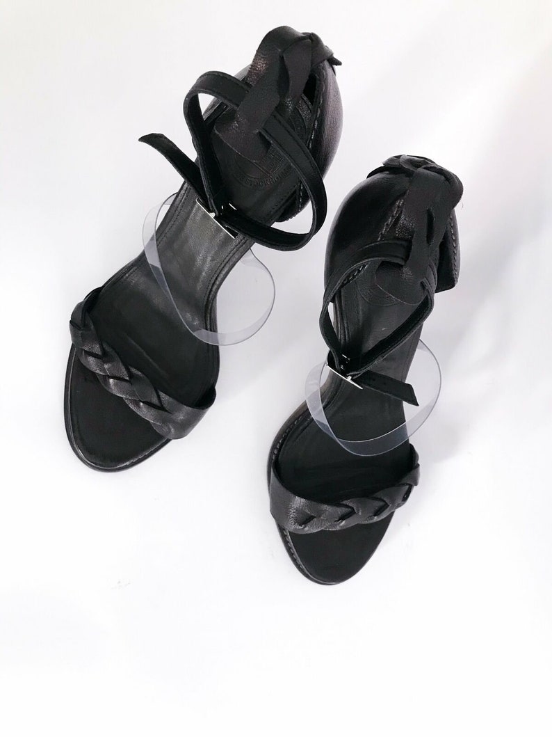 May include: A pair of black leather heeled sandals with braided straps. The sandals have a closed toe and an open heel.
